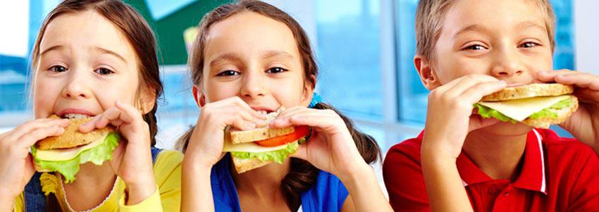 Trois petits enfants mangent des sandwichs